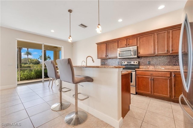 kitchen with light stone counters, stainless steel appliances, a breakfast bar, visible vents, and hanging light fixtures