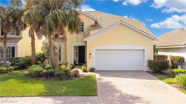 view of front of home featuring a garage, a tile roof, decorative driveway, stucco siding, and a front yard