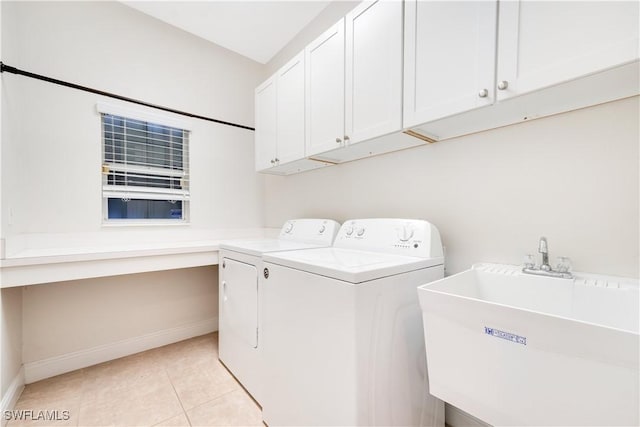 clothes washing area with light tile patterned floors, washing machine and dryer, a sink, baseboards, and cabinet space