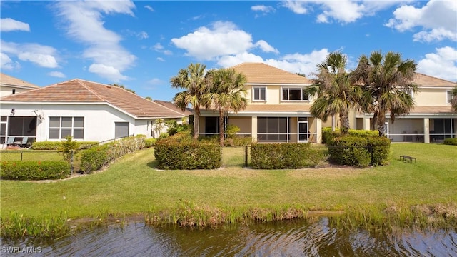 rear view of property with a lawn, a sunroom, a water view, fence, and stucco siding