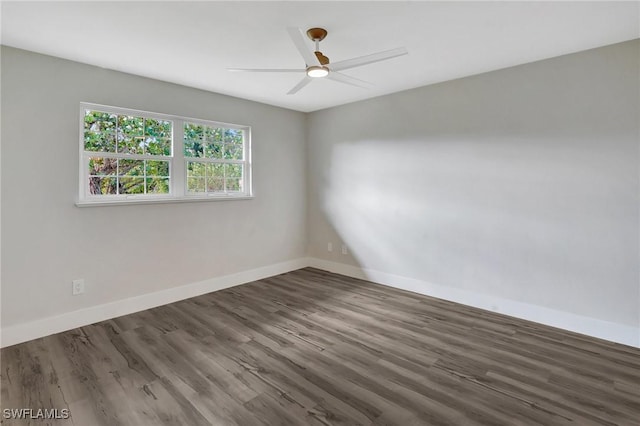 empty room with dark wood finished floors, a ceiling fan, and baseboards