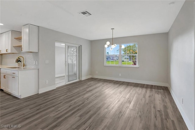 unfurnished dining area with dark wood-style flooring, a sink, visible vents, baseboards, and an inviting chandelier