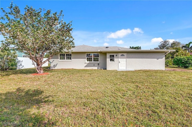 rear view of property featuring a lawn, fence, and stucco siding