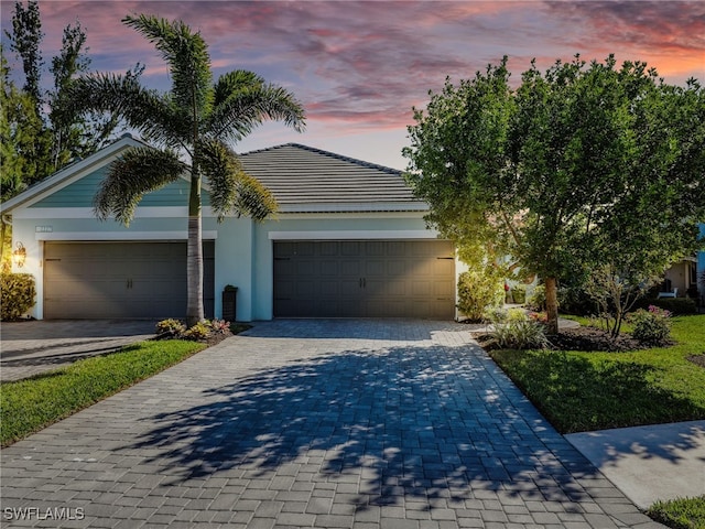 view of front facade with decorative driveway, a tiled roof, an attached garage, and stucco siding