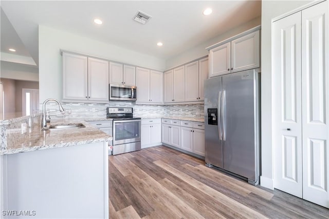 kitchen with a peninsula, a sink, visible vents, appliances with stainless steel finishes, and light stone countertops