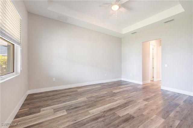 unfurnished room with baseboards, visible vents, a ceiling fan, a raised ceiling, and wood finished floors