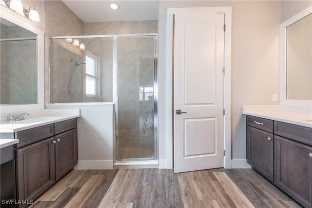 full bath with a sink, two vanities, wood finished floors, baseboards, and a stall shower