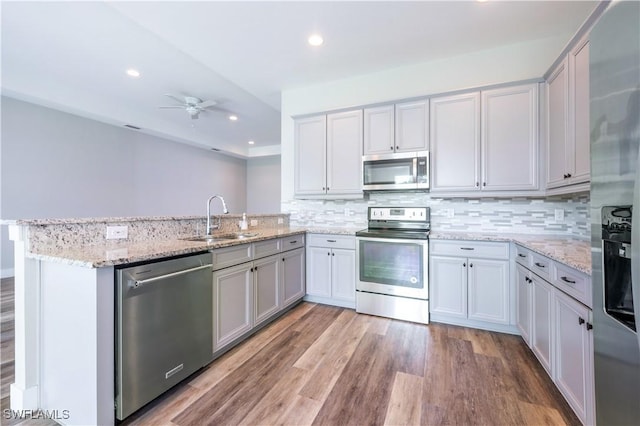 kitchen with stainless steel appliances, light wood-type flooring, a peninsula, and a sink