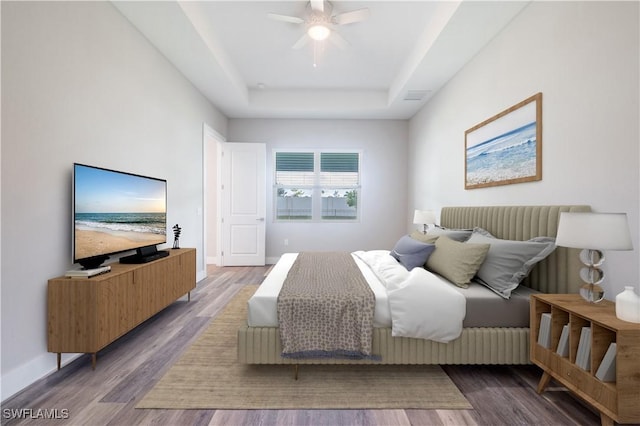 bedroom with baseboards, visible vents, ceiling fan, wood finished floors, and a tray ceiling