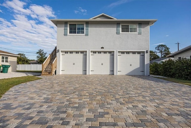 view of front of home featuring decorative driveway, stairway, an attached garage, and stucco siding