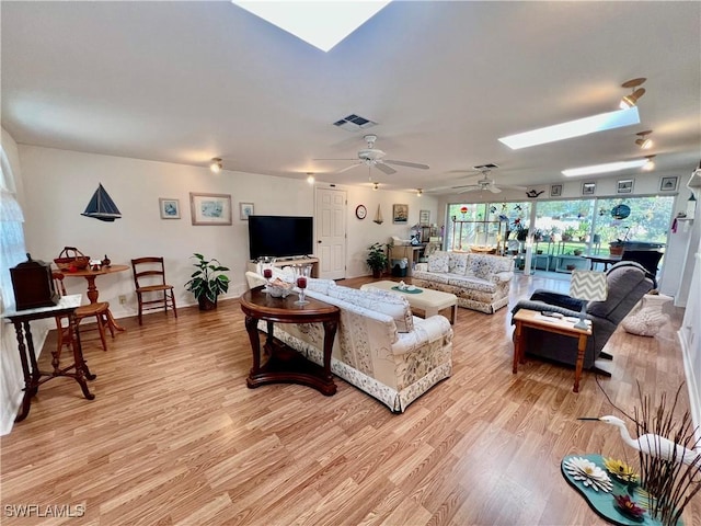 living area with light wood finished floors, a skylight, visible vents, and baseboards