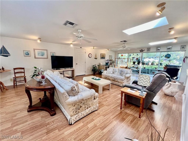 living room featuring ceiling fan, light wood-style flooring, a skylight, and visible vents