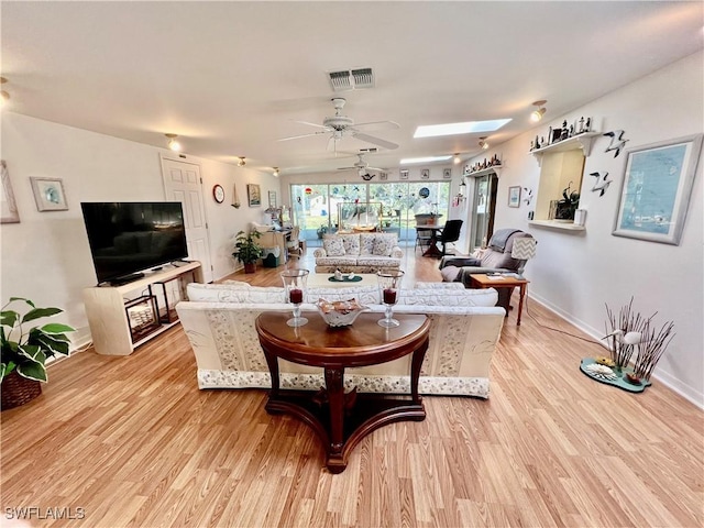 living room with light wood-type flooring, a skylight, visible vents, and a ceiling fan