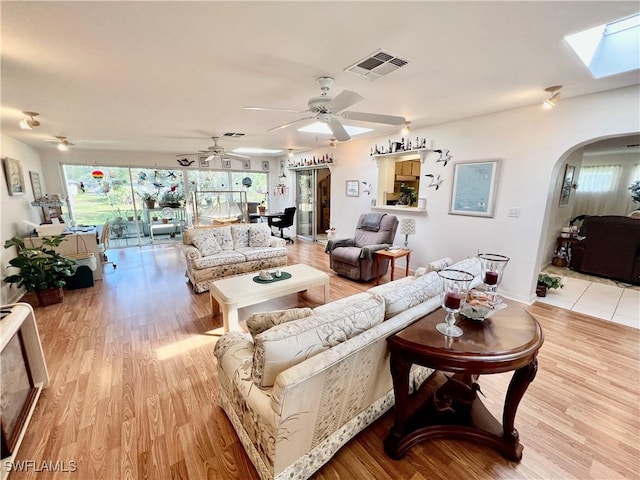 living room featuring arched walkways, visible vents, ceiling fan, and light wood-style flooring