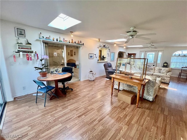 dining space featuring a skylight, light wood-style flooring, baseboards, and a ceiling fan