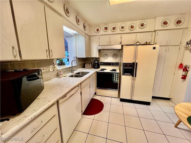 kitchen featuring white appliances, tasteful backsplash, light tile patterned floors, under cabinet range hood, and a sink