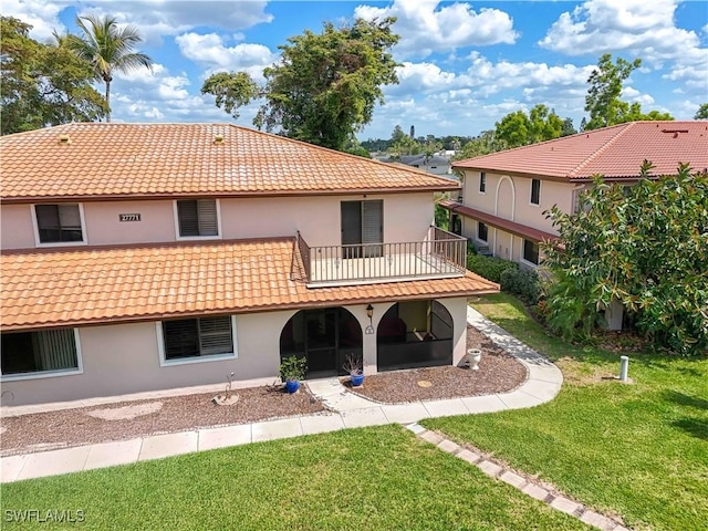 back of house featuring a balcony, stucco siding, a tile roof, and a yard