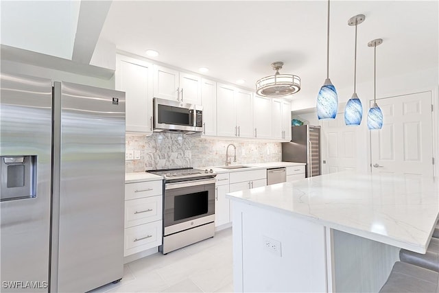 kitchen with stainless steel appliances, a sink, white cabinets, tasteful backsplash, and pendant lighting