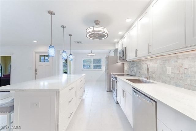 kitchen featuring visible vents, a kitchen island, appliances with stainless steel finishes, a sink, and backsplash