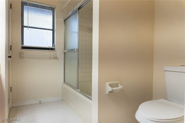 bathroom featuring toilet, tile patterned flooring, baseboards, and combined bath / shower with glass door