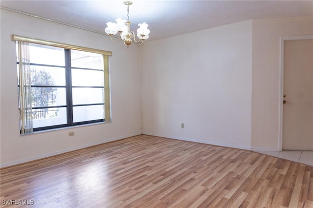 spare room featuring baseboards, light wood-type flooring, and an inviting chandelier