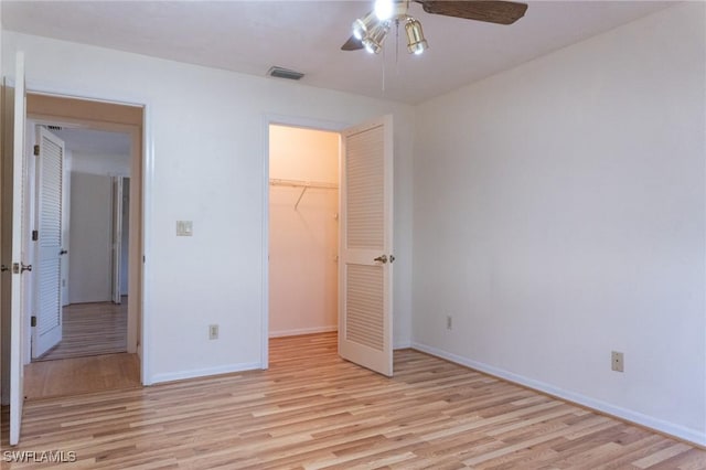 unfurnished bedroom featuring visible vents, baseboards, a closet, light wood finished floors, and a walk in closet