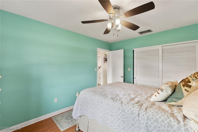 bedroom featuring wood finished floors, a ceiling fan, visible vents, baseboards, and a closet