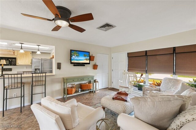 living room with baseboards, visible vents, and ceiling fan