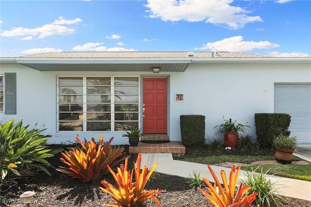 view of exterior entry with a garage and stucco siding