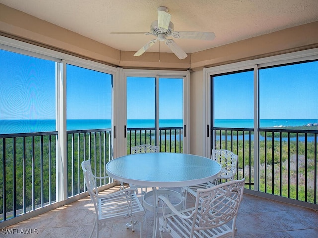 sunroom / solarium featuring a water view, a view of the beach, and a ceiling fan