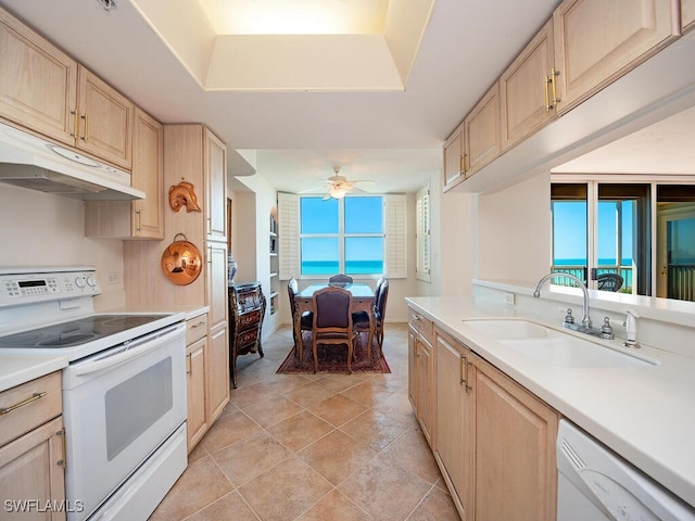 kitchen featuring under cabinet range hood, white appliances, a sink, light countertops, and light brown cabinetry