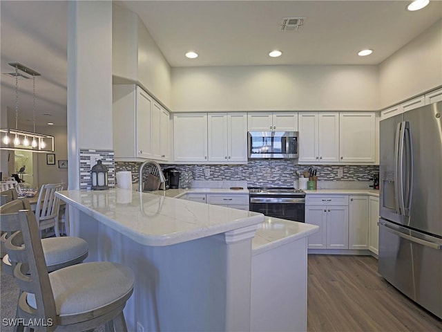 kitchen with pendant lighting, appliances with stainless steel finishes, white cabinetry, light stone countertops, and a peninsula