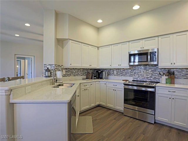 kitchen with dark wood-style flooring, stainless steel appliances, white cabinets, a sink, and a peninsula