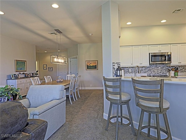 kitchen featuring decorative light fixtures, light countertops, stainless steel microwave, backsplash, and white cabinetry