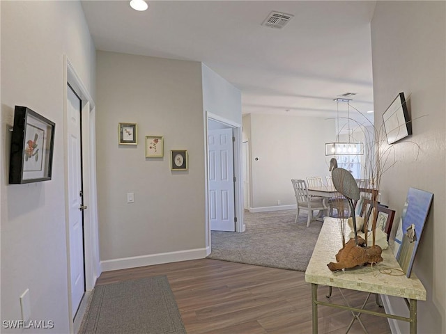 hallway with a notable chandelier, baseboards, visible vents, and wood finished floors