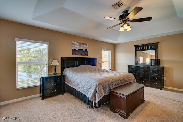 bedroom featuring a ceiling fan, visible vents, baseboards, a raised ceiling, and light colored carpet