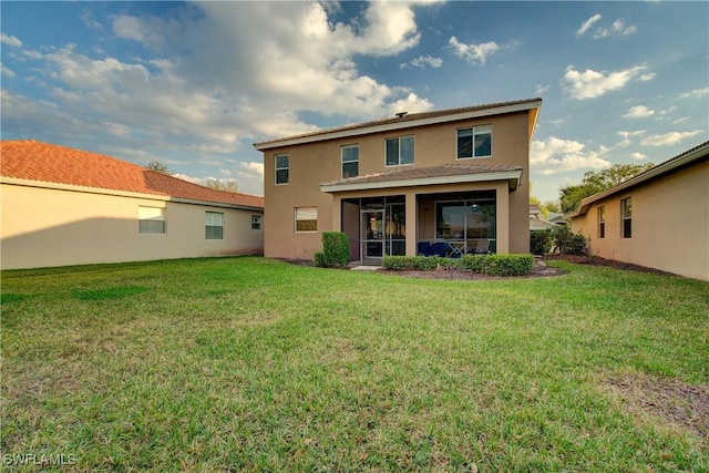 back of house with stucco siding, a lawn, and a sunroom