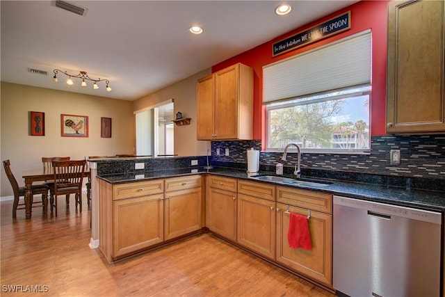 kitchen with a peninsula, a sink, light wood-style floors, dishwasher, and tasteful backsplash