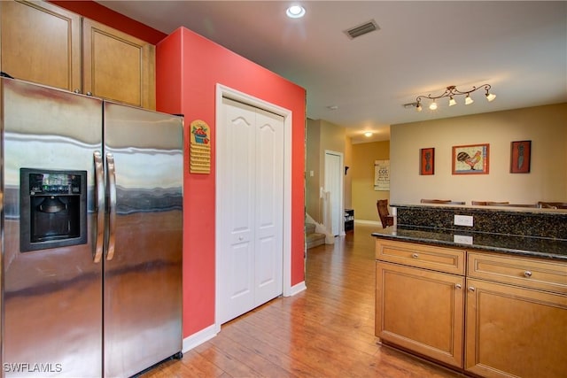 kitchen featuring visible vents, stainless steel refrigerator with ice dispenser, dark stone countertops, light wood finished floors, and baseboards