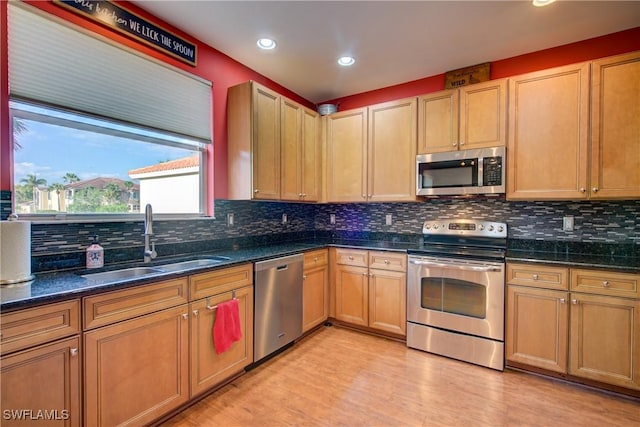 kitchen with light wood-type flooring, decorative backsplash, dark stone countertops, stainless steel appliances, and a sink