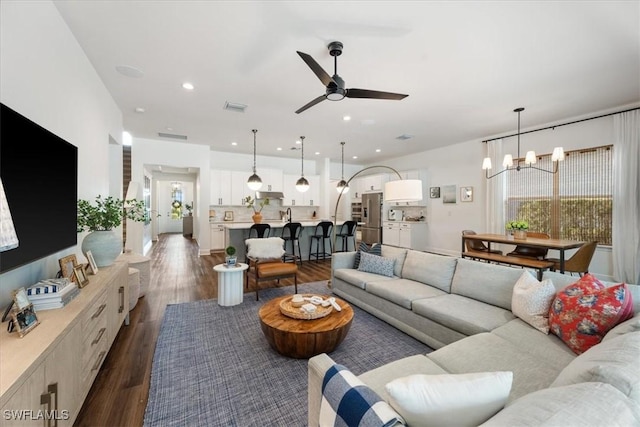 living room with ceiling fan with notable chandelier, dark wood-type flooring, visible vents, and recessed lighting