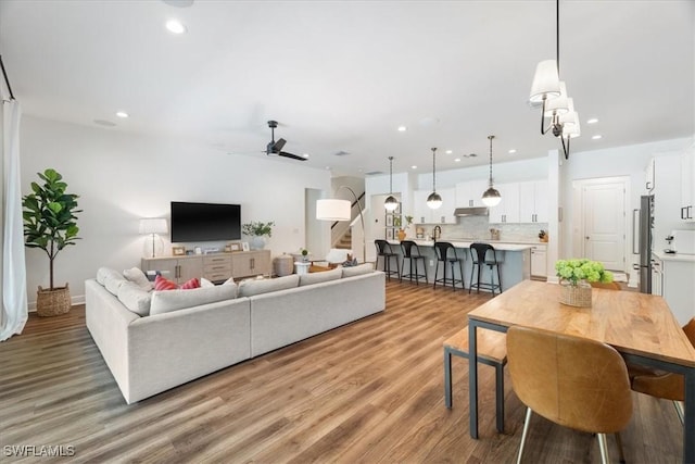 living area with a ceiling fan, stairway, wood finished floors, and recessed lighting