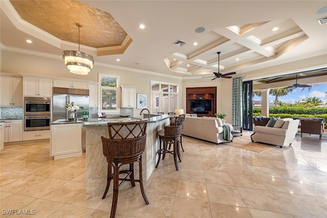 kitchen with a center island with sink, ceiling fan with notable chandelier, coffered ceiling, open floor plan, and stainless steel appliances