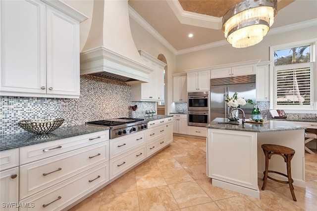 kitchen featuring premium range hood, dark stone counters, a sink, ornamental molding, and stainless steel appliances