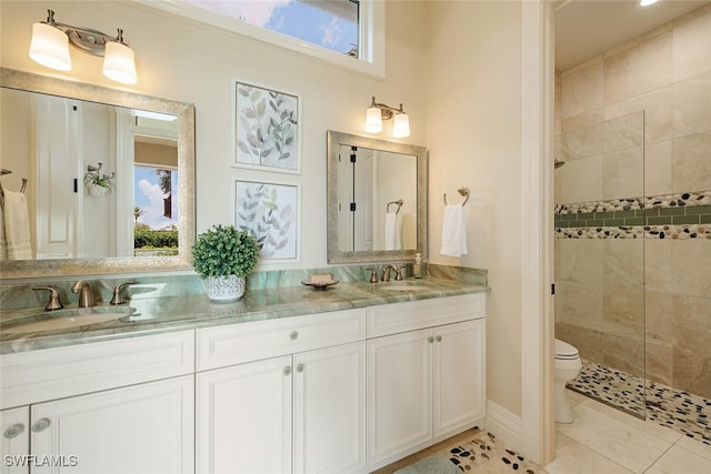 bathroom with a sink, toilet, double vanity, and a tile shower