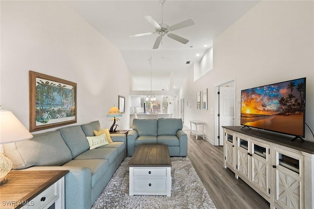 living room featuring a ceiling fan, a towering ceiling, baseboards, and wood finished floors