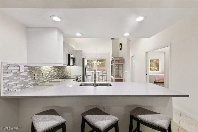 kitchen with white cabinets, appliances with stainless steel finishes, a peninsula, light countertops, and a sink