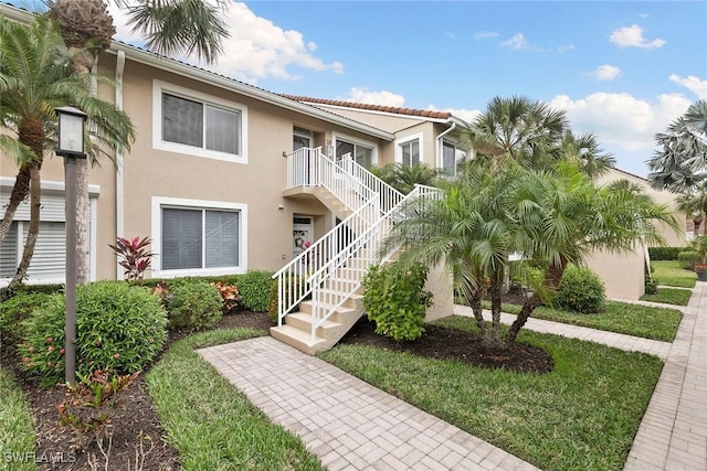 view of property with a front lawn, stairway, and stucco siding