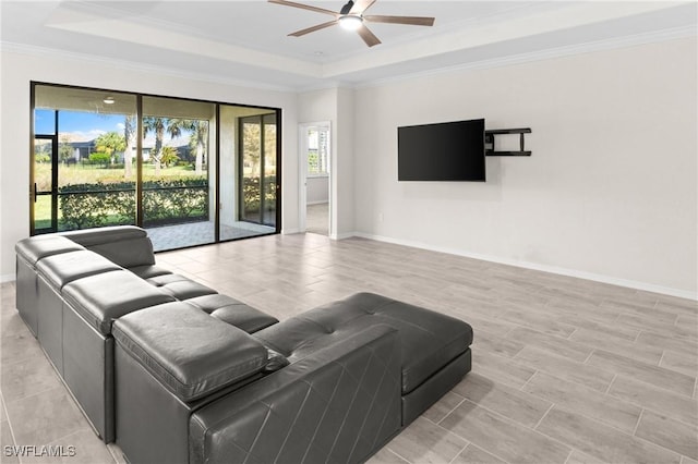 living room featuring a ceiling fan, a tray ceiling, ornamental molding, and baseboards