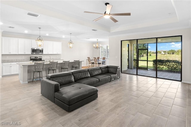 living room featuring ceiling fan with notable chandelier, ornamental molding, a raised ceiling, and visible vents